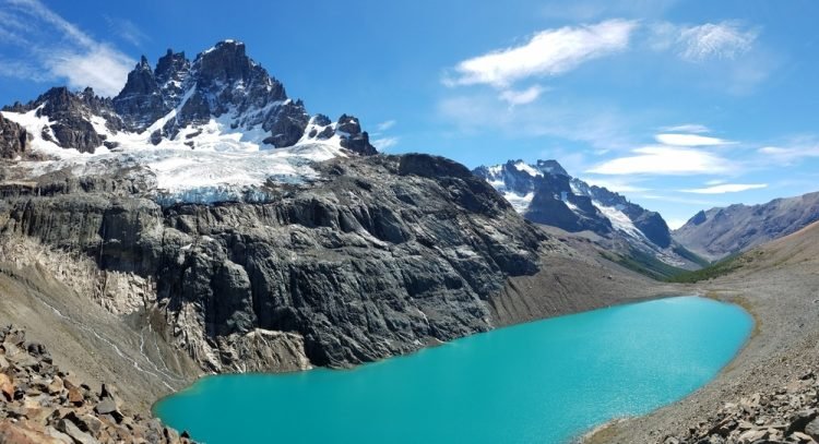 Sunny skies showing a rugged mountain with a glacier over a blue-green glacial lake.