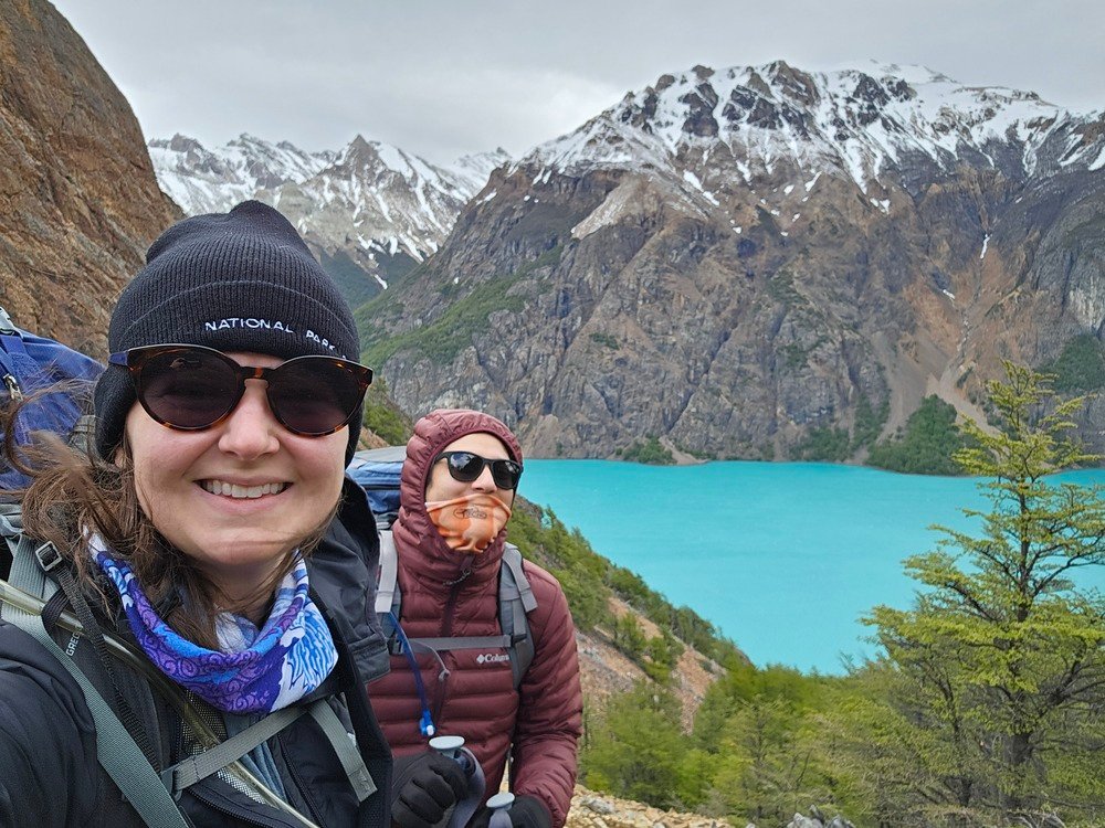 A couple at the top of a mountain pass with turquoise blue water and mountains behind them